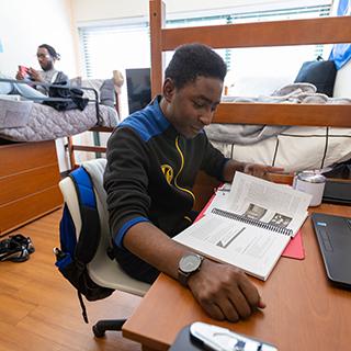 Student studying at a desk in a dorm room. 
