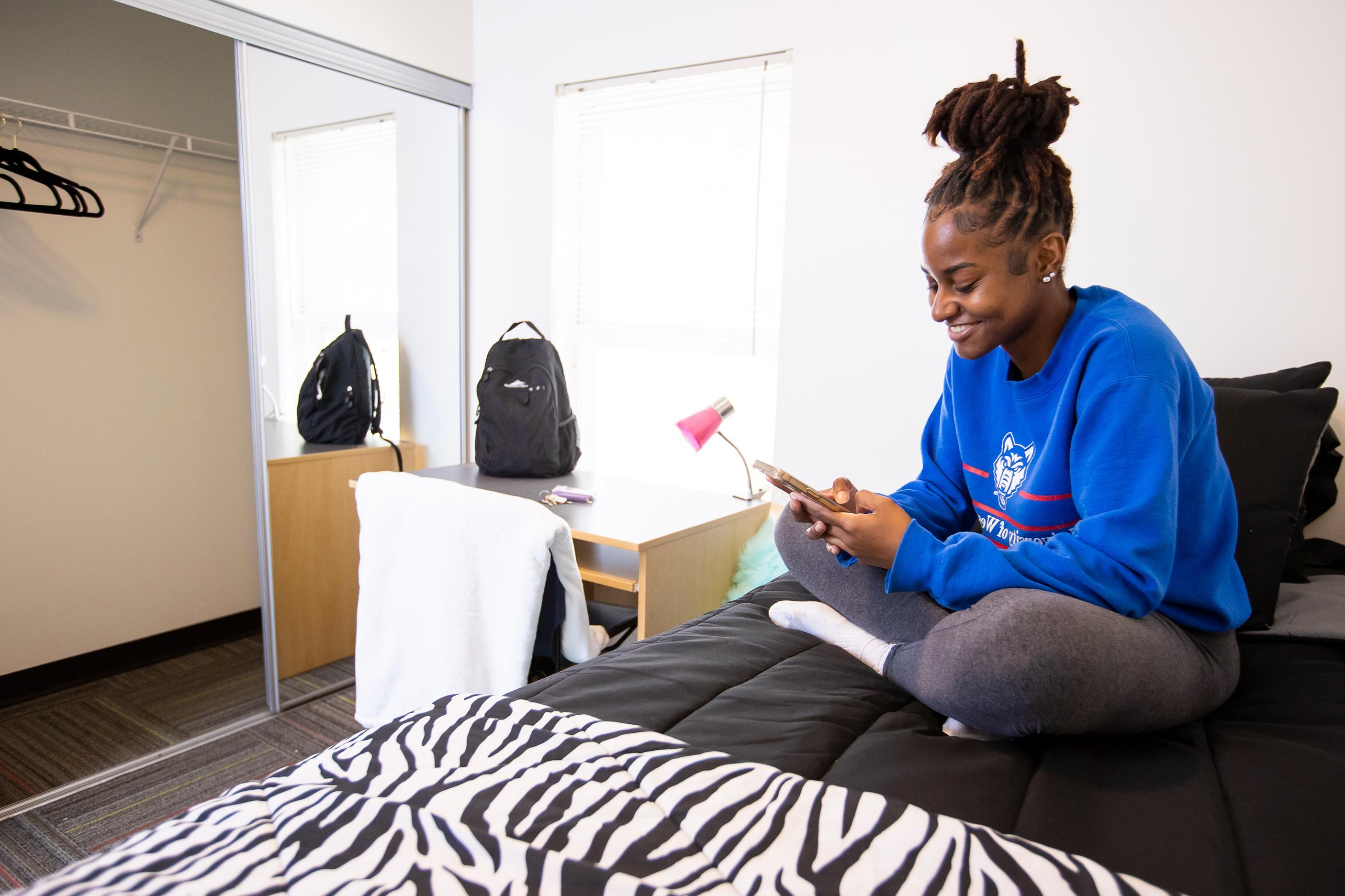 Student in private room looking at phone on bed