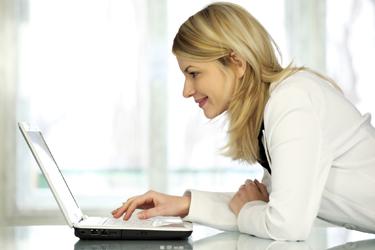 穿白夹克的女人靠在桌子上看着她的笔记本电脑.