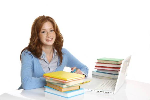 双录取女学生坐在书桌前，手里拿着笔记本电脑和一摞书.